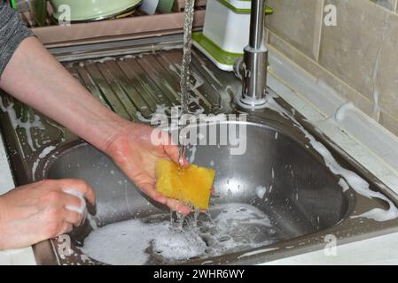 In the picture, a woman's hand washes a washcloth over the sink under running water. Stock Photo