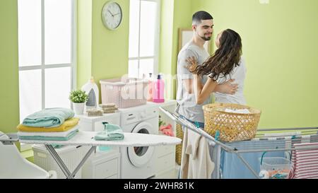 Beautiful couple in love engaging in housework with joy, cheerfully dancing while doing laundry chores together in their home's laundry room Stock Photo