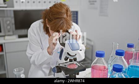 A middle-aged woman working with a microscope in a laboratory setting, surrounded by scientific equipment. Stock Photo