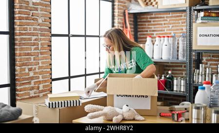 Middle age hispanic woman volunteer smiling confident packing toys on cardboard box at charity center Stock Photo