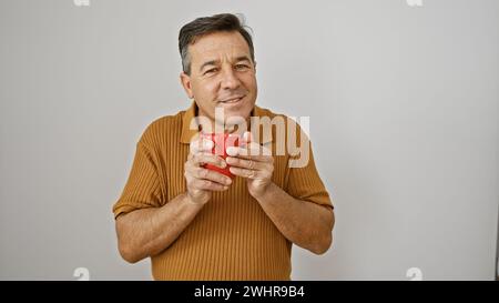 Middle-aged man in sweater holding red mug against white background with content expression. Stock Photo