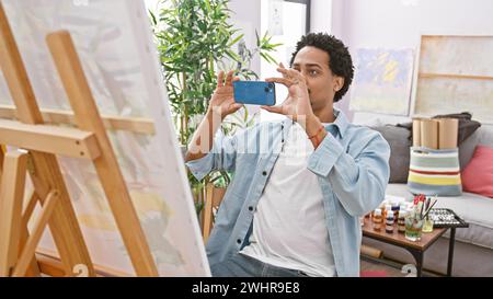 A young man captures his painting on a smartphone in a creative indoor studio setting. Stock Photo
