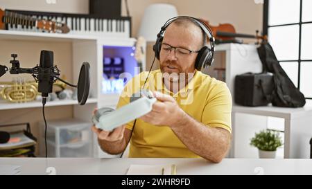 Handsome middle-aged caucasian man musician holding headphones, deeply immersed in a serious video call at his relaxed music studio Stock Photo