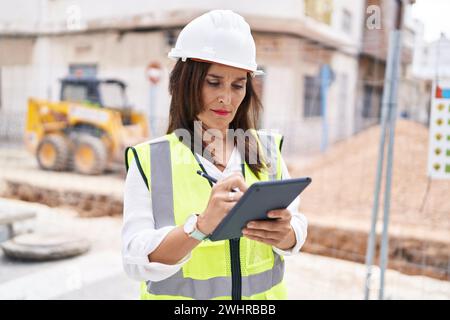 Young beautiful hispanic woman architect drawing on touchpad with relaxed expression at street Stock Photo