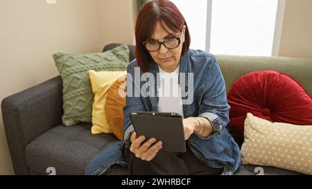 Mature hispanic woman using a tablet on a couch indoors. Stock Photo