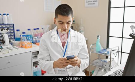 Hispanic male scientist using smartphone in laboratory setting surrounded by medical equipment Stock Photo