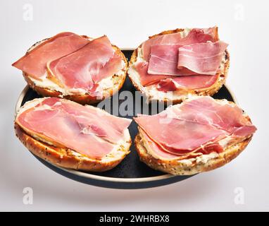 A plate of bagels with cream cheese and prosciutto on a white background. Stock Photo