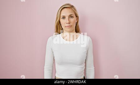 A young blonde woman stands against a plain pink background, exuding a subtle, natural beauty in her casual attire. Stock Photo