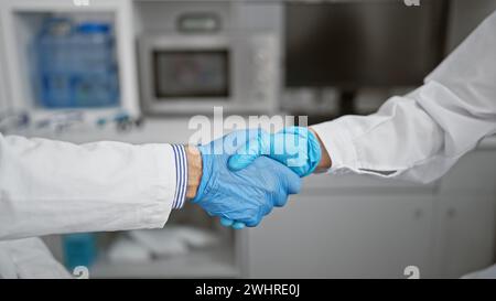 Two enthusiastic scientists shaking hands in agreement, celebrating a groundbreaking medical achievement in their indoor research laboratory. Stock Photo