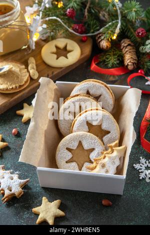 Preparing a homemade sweet present. Linzer Christmas or New Year cookies filled with peanut butter on a dark stone tabletop. Stock Photo