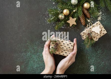 Christmas or New Year layout. Female hands hold Christmas present on a dark green stone background. Holiday concept. Flat lay, c Stock Photo