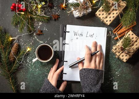 The woman writes in notebook with empty wich list and cup of coffee on xmas dark stone tabletop. New year goals background. Flat Stock Photo