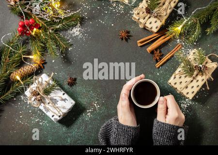Winter concept. Flatlay composition with Christmas presents and female hands hold cup of coffee on a dark stone background. Copy Stock Photo