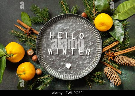 Hello winter text. Winter composition with fir branches, cones and tangerines. Cozy winter mood. Seasons greeting card. Stock Photo