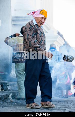 Chichicastenango, Guatemala.  A Cloud of Incense Envelopes a Traditional Quiche Priest as he Swings his Incense Can outside Entrance to Santo Thomas. Stock Photo