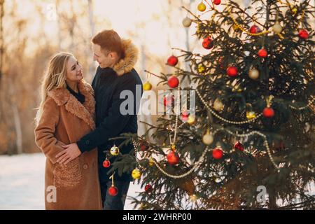 Young adult couple decorates christmas tree in winter forest. New year pine holiday party celebration concept. Stock Photo