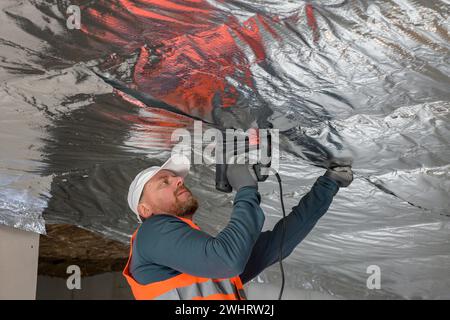the construction worker holds a vapor barrier in his hand - preparation ...