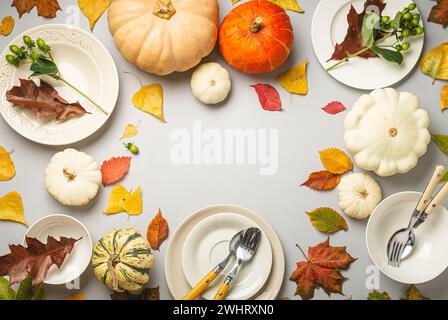 Thanksgiving festive table composition with different colourful pumpkins, autumn leaves, empty plates with cutlery on light grey Stock Photo