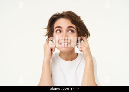 Close up portrait of woman smiling with awkward face expression, shuts her ears, doesnt want to listen, disturbed by loud noise, Stock Photo