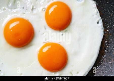 Top view of three of hen eggs being fried in a pan Stock Photo