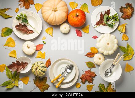 Thanksgiving festive table composition with different colourful pumpkins, autumn leaves, empty plates with cutlery on light grey Stock Photo