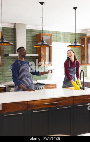 Happy diverse couple cleaning countertop and doing dishes in kitchen at home Stock Photo