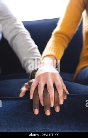Midsection of diverse couple sitting on sofa holding hands at home Stock Photo