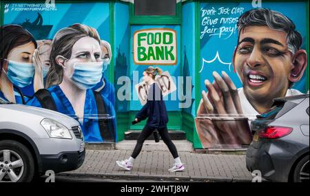 A young woman walking past a shop in Bedminster Bristol UK painted as a food bank with queueing nurses in Don't Just Clap campaign for fair nurses pay Stock Photo