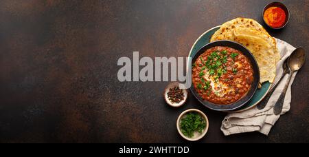 Traditional Indian Punjabi dish Dal makhani with lentils and beans in black bowl served with naan flat bread, fresh cilantro and Stock Photo