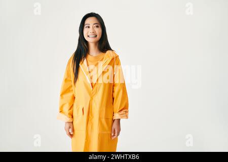 Young smiling asian woman with braces wearing bright yellow raincoat looking aside to copy space Stock Photo