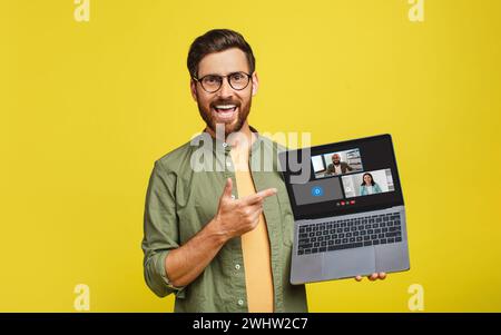 A cheerful man with glasses and a beard excitedly points to a laptop screen displaying Stock Photo