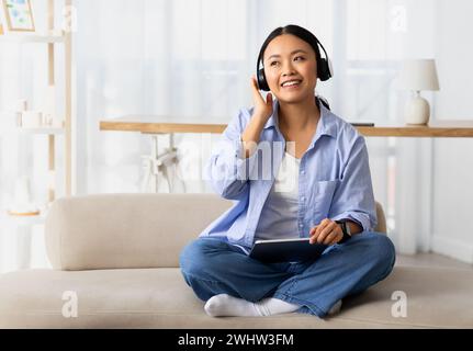 Happy young korean woman using wireless headphones and tablet Stock Photo