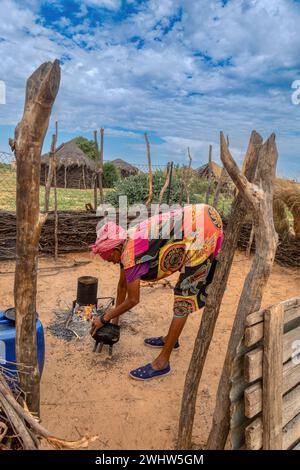 village old african woman cooking in the outdoors kitchen and washing a three legged pot Stock Photo