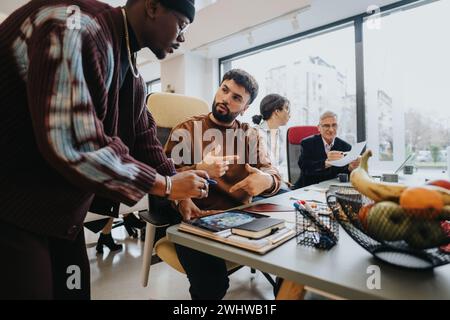 A creative team in a lively discussion at a workplace with a man pointing, a woman drinking coffee, and an elder examining a document. Stock Photo