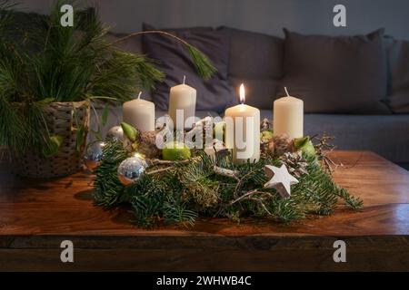 First Advent, wreath with one burning white candle and Christmas decoration on a wooden table in front of the couch, festive hom Stock Photo