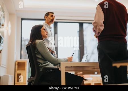 Three business professionals working earnestly at a white desk in a contemporary office setup, deep in discussion over paperwork. Stock Photo