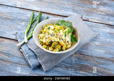 Traditional Greek potato salad with feta cheese and olives served as a close-up in a design bowl on a rustic wooden board with c Stock Photo