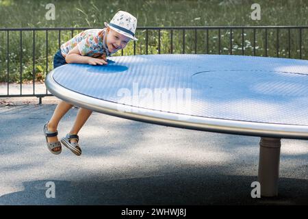 A small, cheerful boy is playing outside, he is trying to climb on a balancing big disc. Stock Photo