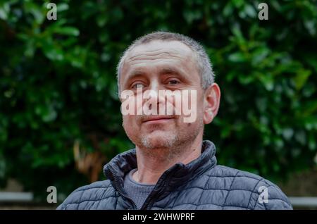 Gray-haired man 45-50 years old in a jacket against a background of greenery. Stock Photo