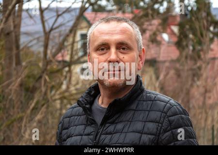 Gray-haired man 45-50 years old in a black jacket on the background of a country house and forest. Stock Photo