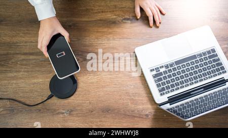 Charging mobile phone battery with wireless charging device in the table. Smartphone charging on a charging pad. Mobile phone ne Stock Photo