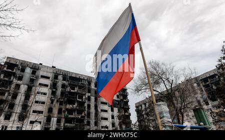 Tricolor flag of Russia against the background of destroyed and burnt houses in Ukraine Stock Photo