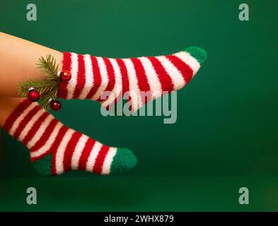 Gils feet in fluffy New Year warm socks. Christmas tree branch with balls decorats female leg Stock Photo