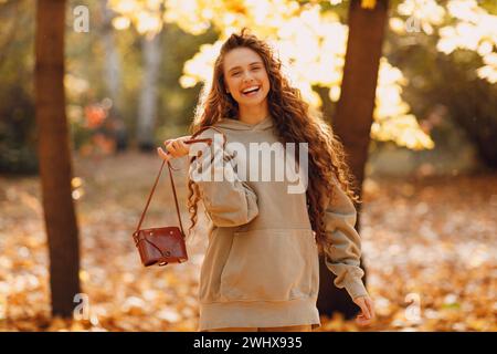 Smiling young woman walking in autumn forest with the yellow leaves at sunset. Stock Photo