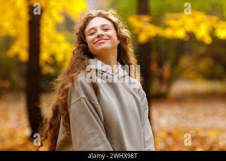 Smiling young woman enjoying the autumn weather in the forest with the yellow leaves at sunset. Stock Photo