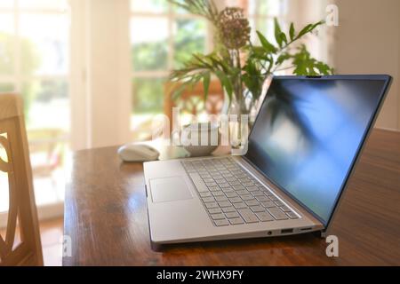Laptop computer on a wooden table with coffee cup and flower bouquet in the dining room, home office working, copy space, select Stock Photo