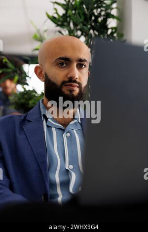 Arab businessman sitting in front of laptop at desk, preparing for video call with clients. Executive manager checking financial analytics report before presentation in coworking space Stock Photo