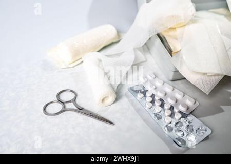 Medical supplies like bandages, plasters, pills and scissors from a first aid kit or home medicine chest on a light gray backgro Stock Photo