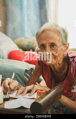 old asian woman writing wording on white paper at home living room Stock Photo