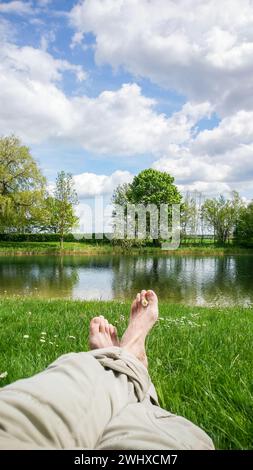 Legs and feet relaxing in front of serene fresh water pond Stock Photo